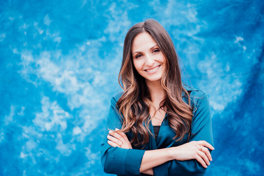 Happy young woman with brown hair standing with arms crossed in front of tie dye backdrop