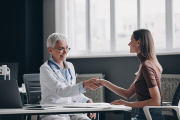 Happy female doctor shaking hands with patient while sitting at the medical office together