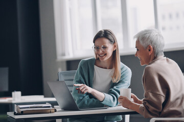 Financial advisor pointing laptop and smiling while discussing options with senior woman in office