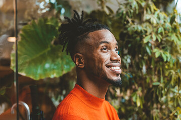 Thoughtful happy young man leaning by glass wall