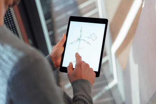 Businessman touching screen of tablet PC with wind turbine drawing in office