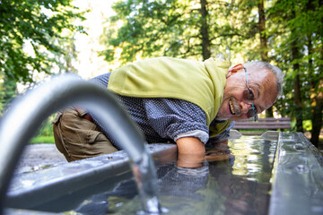 Happy senior man dipping arms in Kneipp basin