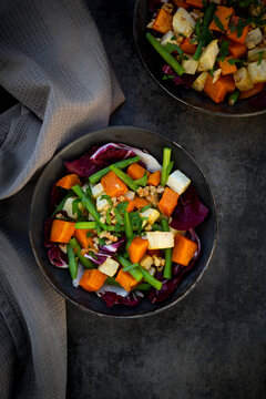 Two bowls of ready-to-eat vegetarian salad with sweet potato, celery, radicchio, green beans, croutons, walnuts and parsley