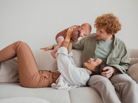 Woman playing with baby boy and man sitting on sofa at home