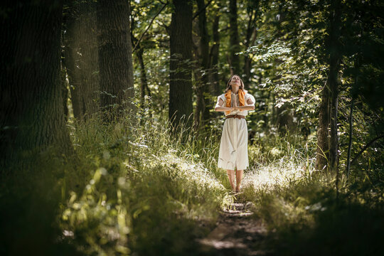Woman with hands clasped standing in forest