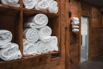Fototapeta na wymiar Clean white towels rolled and stacked in shelf of sauna in luxury hotel SPA. Luxury travel concept