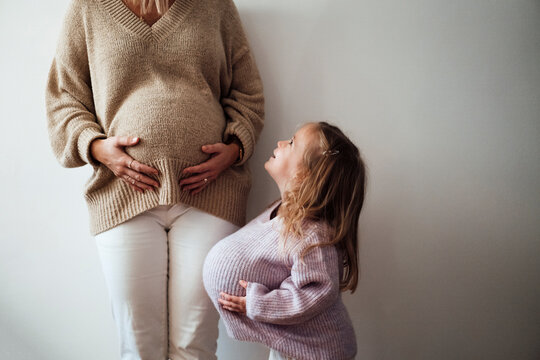 Daughter imitating mother's pregnancy in front of wall