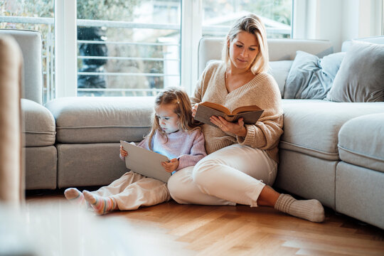 Mother reading book by daughter using tablet PC at home
