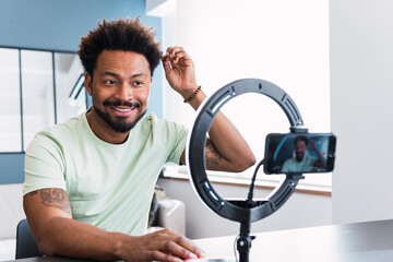 Smiling man with hand in hair making tutorial through smart phone at home