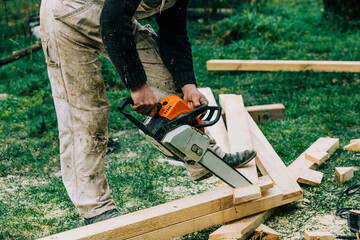Carpenter cutting wood with chainsaw on grass
