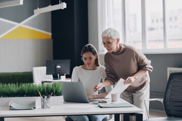 Obraz premium Two confident businesswomen looking at computer monitor while working in the office together