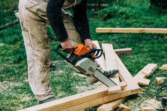 Carpenter cutting wood with chainsaw on grass