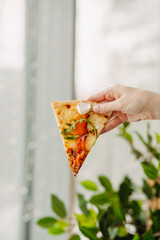 A piece of pizza in his hand, against the backdrop of the restaurant, Side view of the pizza. The concept of Italian cuisine, street food, fast food, fast food. Banner