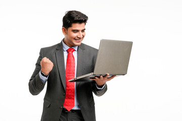 Young indian businessman in suit, holding laptop and giving a winning expression.
