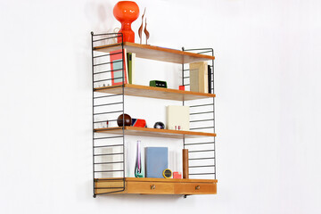 a mid century String Shelf with drawers original from the 60s mounted on a white wall with books...