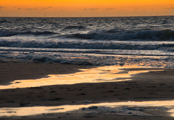 Fototapeta na wymiar Nordsee direkt an der Küste und Wasserlinie mit Wellen und Brechern und der Horizont im glühenden Sonnenuntergang