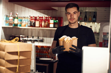 Man is standing and holding French fries that is in the paper eco boxes