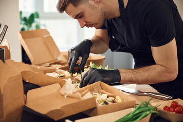 Vegetables added to the burgers. Man is packing food into the paper eco boxes. Indoors, restaurant