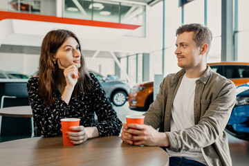 Buying a new car. A young couple drinks coffee. Registration of documents for a car