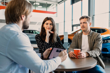 A sales manager with a tablet is sitting at a table with a couple who came to buy a new car. Consultation before purchase