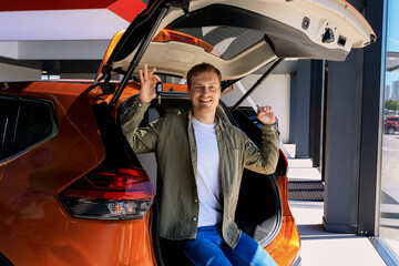 Naklejka premium A man is sitting in the trunk of his car with a key in the showroom of a dealership.Happy car buyer. Emotions from the purchase