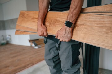 Plank is in the hands. Man is installing new laminated wooden floor