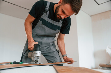 Using the electric machine tool to cut the plank. Man is installing new laminated wooden floor