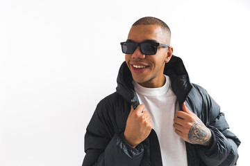 Studio shot of confident street style loving man in sunglasses, putting on his black puffer jacket...