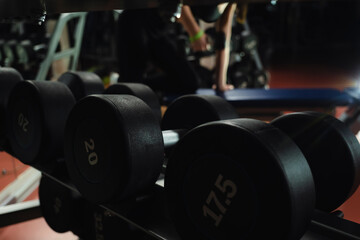 a woman lifts a dumbbell in the background. heavy black metal dumbbells for strength training on the rack. lifting dumbbells