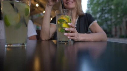 Close-up healthful drink in glass with happy smiling unrecognizable woman stirring cocktail. Relaxed Caucasian lady sitting in cafe with juice enjoying leisure on vacations