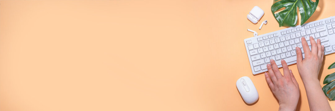 Summer office background with keyboard. Simple minimal beige flatlay with tropical monstera leaf, white keyboard, mouse, earphones, top view copy space