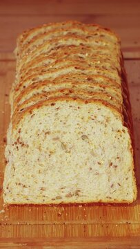 Vertical video social media format – Closeup of a man’s hand taking the end two slices of freshly baked bread from a fresh loaf with added seeds.