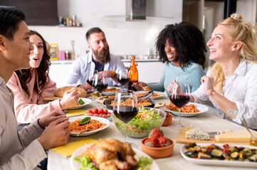 Happy group of friends eating spaghetti pasta with red tomato sauce at home dinner party, cheerful young people having lunch break together