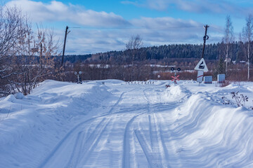 Countryside road crosses railroad track at winter day.