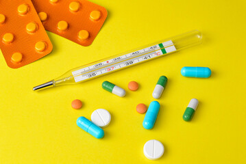 Colourful different pills and medical thermometer on yellow surface