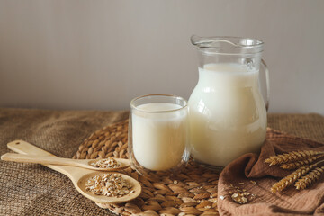 Milk in a jug and a glass, a wooden spoon with oatmeal and ears of wheat on the table
