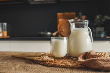 Milk in a jug and a glass, a wooden spoon with oatmeal and ears of wheat on the table
