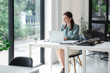 Young confident businesswoman sitting at the office table working on laptop computer