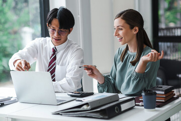 Young confident business people sitting at the office table working on laptop computer with...