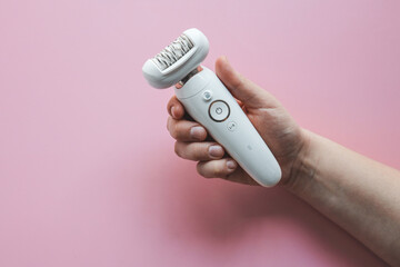Woman holding a stylish epilator in her hand on a pink background