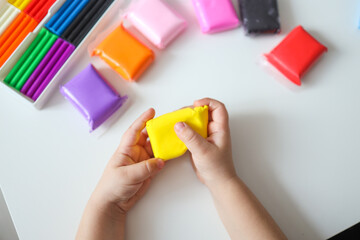 Child hands molding modeling clay or plasticine on white table