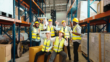 Multiracial warehouse workers in safety wear are dancing to relax after working hard on shipping goods. Male and female logistic employees are spending time together to celebrate the success of jobs.