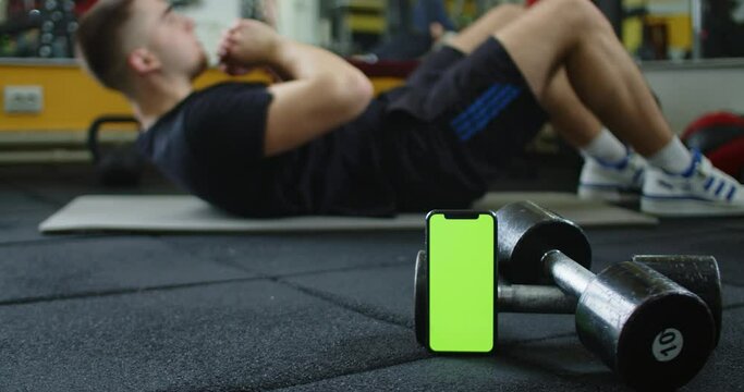 A video featuring a green screen smartphone and a man doing ab exercises in the background. This footage can be used to add customized text, images, or videos to the green screen area to create an eye