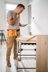 Hard working carpenter standing in front of his work desk , reading blueprint and thinking about the project