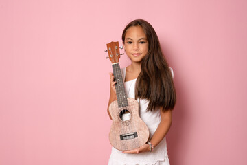 Little girl plays ukulele. Creative development in children. Musical education from childhood....