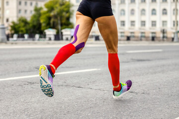 legs female runner in compression socks and kinesio tape on knee to running marathon, woman jogger run city race