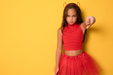 Closeup photo of funny little lady with long hair and headband playing helloween party satan devil character wear read costume with thumb down isolated yellow color background