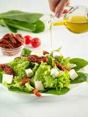 Salad of sun-dried tomatoes, cheese and salad leaves. Olive oil pouring on salad