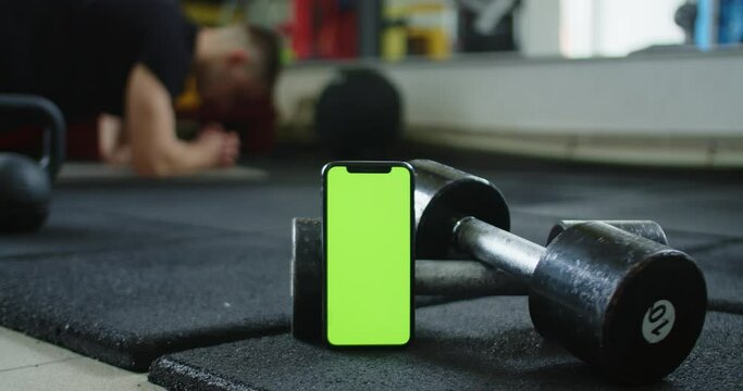 A video featuring a green screen smartphone and a man doing ab exercises in the background. This footage can be used to add customized text, images, or videos to the green screen area to create an eye
