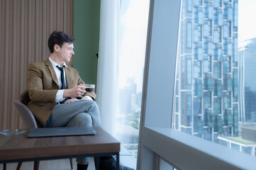 Young businessman sit and relax in the relaxation room by the window overlooking the beautiful city buildings.